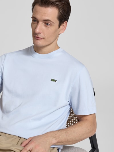 Męski model nosi Regular Fit Poloshirt aus reiner Baumwolle von Lacoste, jednokolorowy, wyhaftowane logo, okrągły dekolt, krótki rękaw, bawełna, jasnoniebieski kolor, Ganzkörperansicht z przodu.