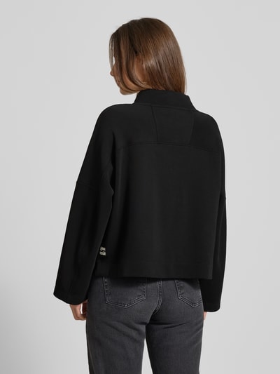 Frauenmodel trägt Oversized Sweatshirt mit Tunnelzug von Marc Cain aus schwarzem Baumwoll-Mix mit Stretch-Anteil, Stehkragen, Ganzkörperansicht Rückansicht.