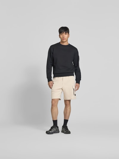 Männermodel trägt Shorts mit elastischem Bund von Moose Knuckles, Cargo-Taschen, Logo-Detail, beige, gerade Form, Ganzkörperansicht von vorne.