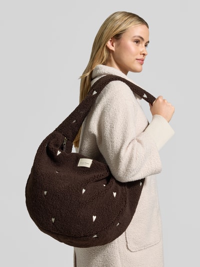 Vrouwenmodel draagt Bauchtasche aus Teddyfell van Studio Noos in donkerbruin met witte stikselmotieven, brede schouderriem, hoofdvak en binnenvak met rits, afmetingen 58x38x11 cm, schouderriem 76 cm, materiaal met zachte textuur, detailopname zijaanzicht