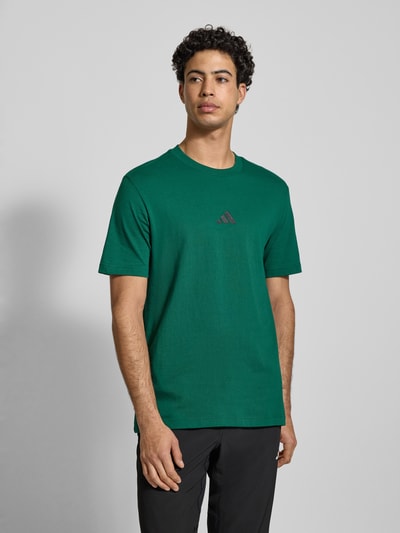 Männermodel trägt T-Shirt mit Label-Print von adidas Sportswear in Grün, Reine Baumwolle, Regular-Fit, Rundhalsausschnitt, Ganzkörperansicht von vorne. Rückenlänge bei Größe M: 75 cm.