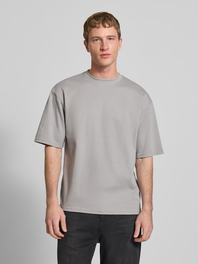 Männermodel trägt Boxy Fit T-Shirt aus Baumwoll-Mix Modell 'CASPIAN AIRFLEX BOXY' von Only & Sons in Optik: Unifarben, Ganzkörperansicht von vorne. Passform: Boxy-Fit, Rundhals-Ausschnitt, Kurzarm, Airflex, kühlend, atmungsaktiv, feuchtigkeitsregulierend.