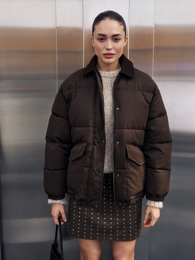 Kobieta modelka nosi kurtkę pikowaną z wykładanym kołnierzem i listwą na zamek błyskawiczny Steppjacke mit verdeckter Reißverschlussleiste von Jake*s Casual, krój regular fit, kieszenie z patką, długość tyłu 70 cm, szerokość ramion 50 cm, szerokość klatki piersiowej 62 cm, długość rękawów 56 cm, stylizacje casualowe; całkowity widok z przodu.