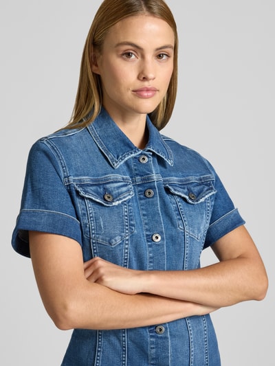 Frauenmodel trägt Jeanskleid mit Fransensaum und Knopfleiste von Liu Jo White, blaue Denim-Optik, Brusttaschen, Nahaufnahme Oberkörper.