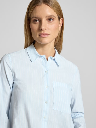 Frauenmodel trägt Regular Fit Hemdbluse mit Brusttasche Modell 'Darma' von Vila aus Baumwoll-Mix, hellblau-weiß gestreift, Nahaufnahme Oberkörper.