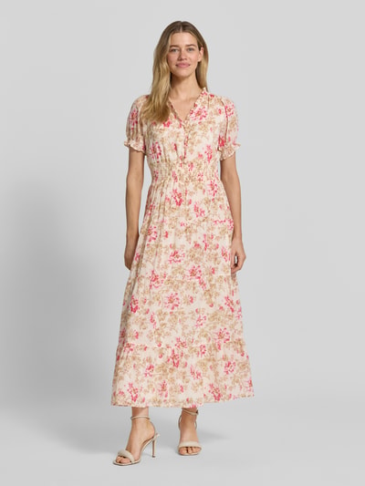Frauenmodel trägt Maxikleid mit floralem Allover-Print Modell 'Kanza' von Neo Noir aus Reine Baumwolle mit Rüschenbesatz, V-Ausschnitt, Smok-Detail, taillierte Passform, kurzärmelig, Farbmix aus Beige und Pink, leicht strukturierte Textur, Ganzkörperansicht von vorne.
