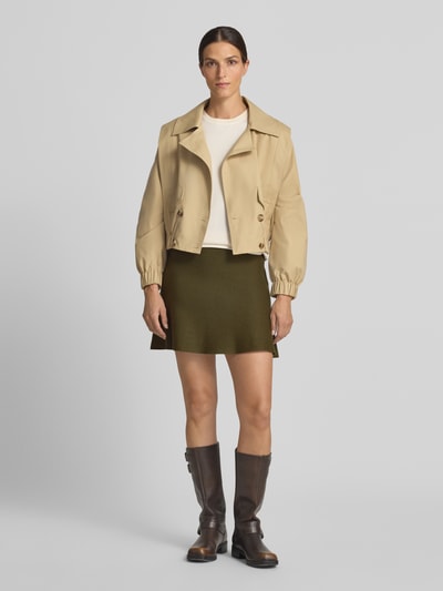 Frauenmodel trägt ausgestellten Mini-Rock aus Viskose-Baumwoll-Mix Modell 'ELLY' von VERO MODA in Olivgrün, unifarben, Feinstrick, Ganzkörperansicht von vorne.