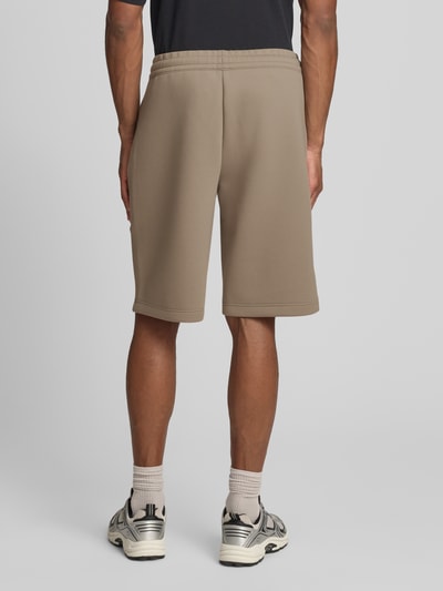 Männermodel trägt Bermudas mit Reißverschlusstaschen von EA7 Emporio Armani aus Material-Mix mit Viskose-Anteil, Regular-Fit, elastischer Bund, Farbe Beige, Ganzkörperansicht Rückansicht.