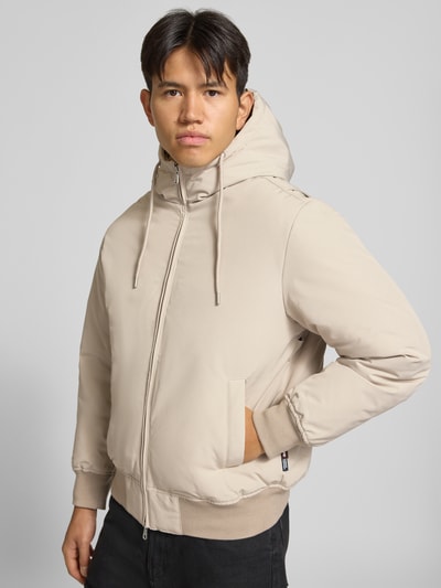 Männermodel trägt Jacke mit Kapuze und Eingrifftaschen Modell 'TRACE' von JACK & JONES in Beige, Regular Fit, Ganzkörperansicht von vorne.
