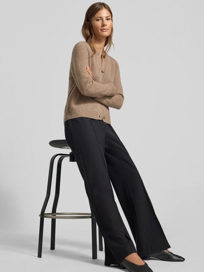 Frauenmodel trägt Strickjacke aus reinem Kaschmir von MYON in Beige, kombiniert mit dunkler Hose; glatte Textur, Ganzkörperansicht von vorne. Gerade Passform, Rundhalsausschnitt, durchgehende Knopfleiste, Rückenlänge 56 cm, Ärmellänge 66 cm.