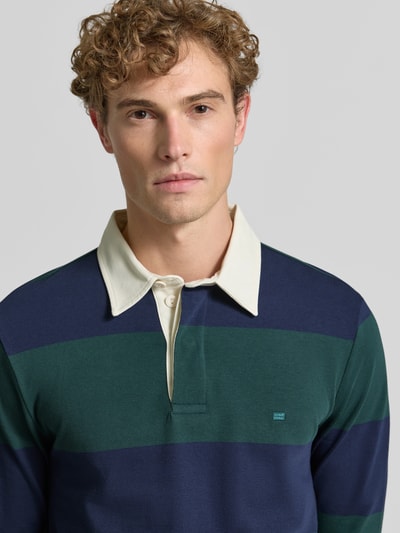 Männermodel trägt Poloshirt aus reiner Baumwolle von Christian Berg Men in Dunkelgrün und Dunkelblau, lockere Passform, Nahaufnahme Oberkörper.