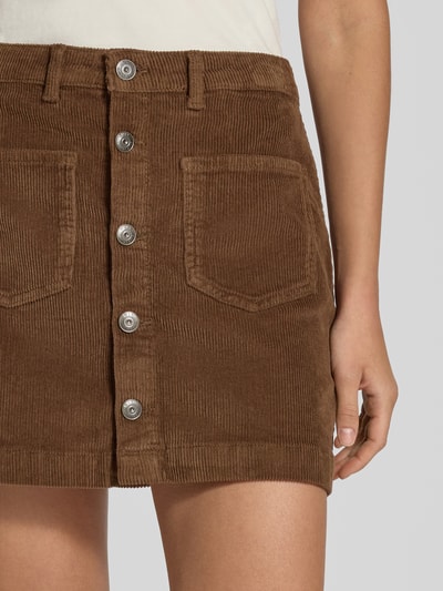 Frauenmodel trägt Eng anliegender Mini-Rock aus Baumwoll-Mix Modell 'AMAZING' von ONLY in Braun mit sichtbaren Knöpfen und Taschen, Nahaufnahme Oberkörper. Damen Mini-Rock von ONLY.
