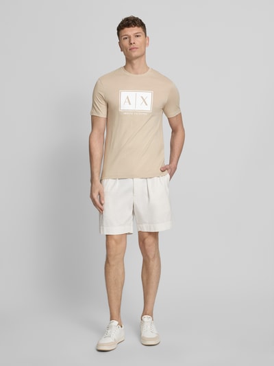 Männermodel trägt T-Shirt mit Logo und Rundhalsausschnitt von ARMANI EXCHANGE aus reiner Baumwolle, Regular-Fit, beiger Farbton, Ganzkörperansicht von vorne. Rückenlänge bei Größe M: 71 cm.