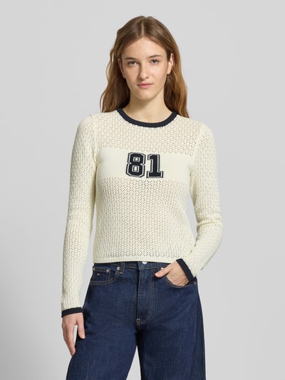 Frauenmodel trägt Slim Fit Pullover in Strick-Optik von Guess Jeans, semitransparent, cremefarben mit dunklen Bündchen, Nahaufnahme Oberkörper.