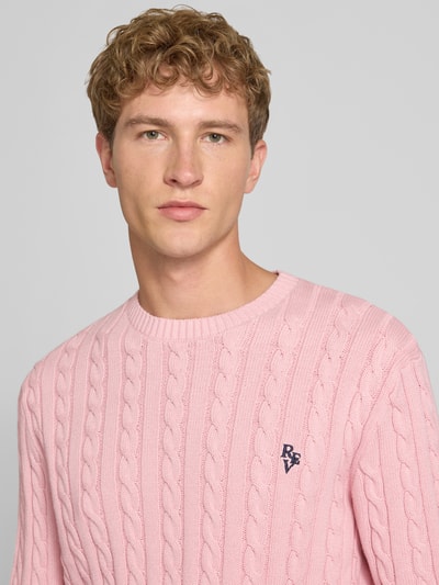 Männermodel trägt Slim Fit Strickpullover reine Baumwolle von REVIEW in Rosa mit Zopfmuster, Logo-Stickerei, Nahaufnahme Oberkörper.