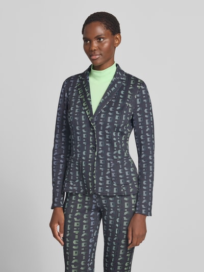 Frauenmodel trägt Slim Fit Blazer mit Logo-Detail von Marc Cain in Dunkelblau mit grünem Muster, elastischer Material-Mix, Nahaufnahme Oberkörper.