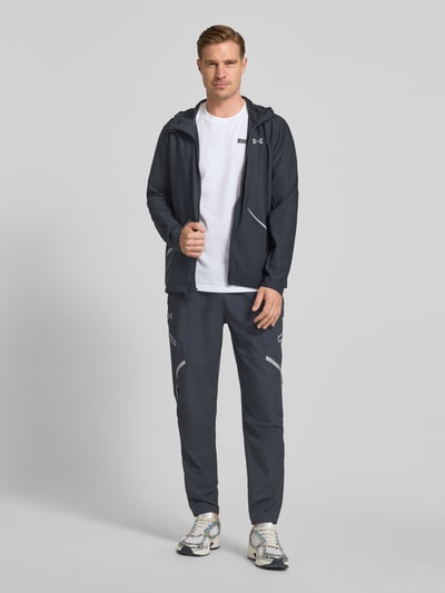 Männermodel trägt Regular Fit Jacke mit Logo-Print Modell 'Unstoppable' von Under Armour in Dunkelgrau, glatte Textur, Ganzkörperansicht von vorne, elastischer Material-Mix, mit Kapuze, Reißverschluss und Reißverschlusstaschen.