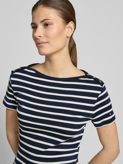 Frauenmodel trägt Slim Fit T-Shirt aus reiner Baumwolle von Tommy Hilfiger, dunkelblau-weiß gestreift, Logo-Detail, Zierknöpfe, Nahaufnahme Oberkörper.