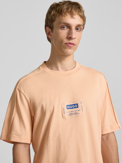 Männermodel trägt Regular Fit T-Shirt aus reiner Baumwolle Modell 'NURAZTI' von Hugo Blue in Apricot mit Label Patch, Nahaufnahme Oberkörper.