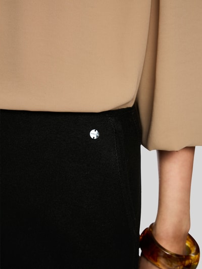 Frauenmodel trägt Midirock aus Schurwolle mit Reißverschluss von Marc Cain, schwarze A-Linie, Teilungsnaht, Label-Detail, Nahaufnahme Oberkörper.