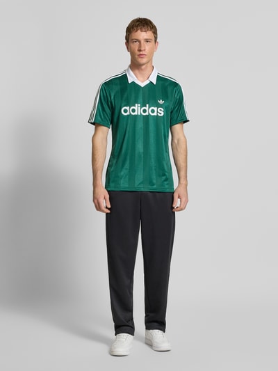 Männermodel trägt Trikot mit Umlegekragen und Label-Print von adidas Originals, Regular-Fit, V-Ausschnitt, Ganzkörperansicht von vorne.