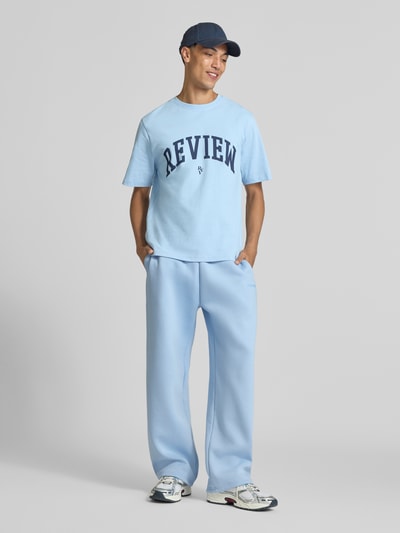 Männermodel trägt hellblaue Straight Fit Sweatpants Baumwoll-Mix von REVIEW mit seitlichen Taschen, elastischem Bund und Gesäßtasche, Ganzkörperansicht von vorne.