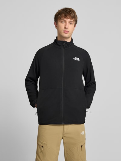 Männermodel trägt Jacke mit Raglanärmeln und Logo-Print Modell 'PACKABLE KECHA' von The North Face, Material-Mix mit Stretch-Anteil, Gerader-Schnitt, Schwarz, Stehkragen, Reißverschluss, Rückenlänge 68 cm, Ärmellänge 72 cm, Ganzkörperansicht von vorne.