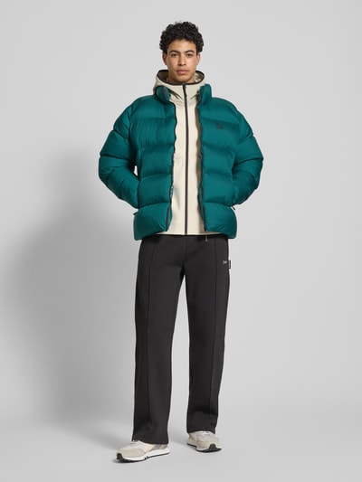 Männermodel trägt grüne Steppjacke mit Label-Print von PUMA PERFORMANCE, unifarben, gerader Schnitt, Reißverschlusstaschen, Ganzkörperansicht von vorne.