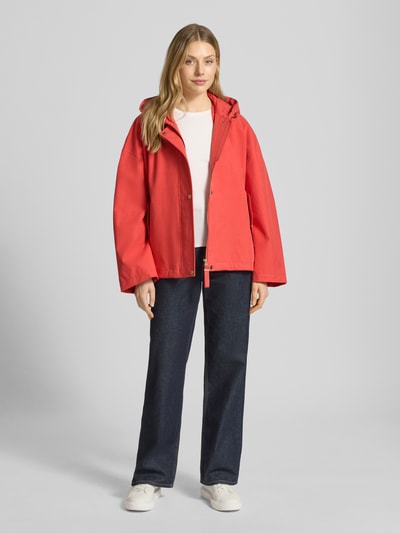 Frauenmodel trägt Jacke mit Kapuze und versiegelten Nähten Modell 'ELLE' von G-LAB aus Lyocell-Mix mit Leinen-Anteil, Gerader-Schnitt, Wasserdicht, Winddicht, Atmungsaktiv, Reiß- und Druckknopfverschluss, seitliche Pattentaschen, rote Farbe, glatte Textur; Ganzkörperansicht von vorne.