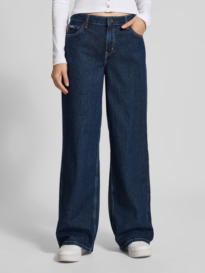 Frauenmodel trägt Wide Fit Jeans mit Logo-Patch von GUESS, dunkles 5-Pocket-Design, Knopf- und Reißverschluss, Ganzkörperansicht von vorne.