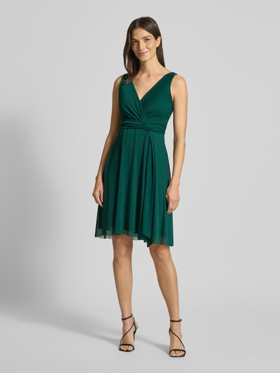 Modelka kobieca nosi zielone cocktailkleid mit V-Ausschnitt von TROYDEN COLLECTION, taliowany krój, pasek w talii, całościowy widok z przodu.