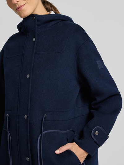 Vrouwenmodel draagt Regular Fit lange wollen jas van zuiver wol met opstaande kraag, tunnelkoord, opgestikte steekzakken, knoopsluiting van Marc Cain, ruglengte maat 36: 78 cm, schouderbreedte 46 cm, borstwijdte 41 cm, mouwlengte 56 cm, close-up bovenlichaam.