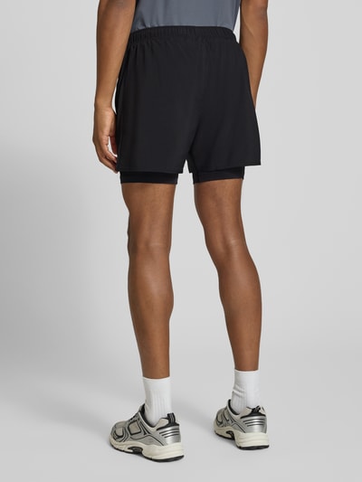 Männermodel trägt schwarze Shorts im 2-in-1-Look mit Logo von ASICS, elastischer Bund, Regular Fit, Ganzkörperansicht Rückansicht.