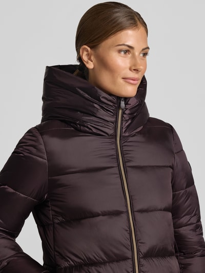 Frauenmodel trägt Steppmantel mit Kapuze Modell 'LYSA' von Save The Duck in Dunkelviolett, glatte Struktur, Nahaufnahme Oberkörper. Gerader Schnitt, Zweiwege-Reißverschluss, Label-Patch, seitliche Eingrifftaschen, Kontext: Damen Steppmantel Save The Duck.