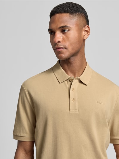 Männermodel trägt Regular Fit Poloshirt aus reiner Baumwolle Modell 'DONOS222' von HUGO, sandfarben, Label-Applikation, Nahaufnahme Oberkörper.