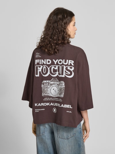 Modelka nosi Oversized T-Shirt mit Rundhalsausschnitt od Karo Kauer, bawełna, krój oversized, nadruk z logo, okrągły dekolt, długość tyłu 59 cm; widok całej sylwetki z tyłu.