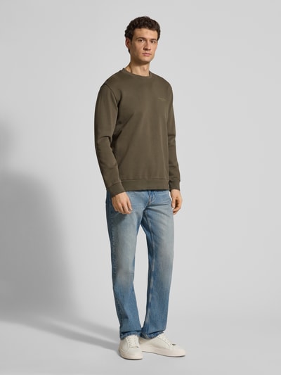 Männermodel trägt Regular Fit Sweatjacke aus reiner Baumwolle von Marc O'Polo, olivgrün, unifarben, gerippte Abschlüsse, Ganzkörperansicht von vorne.