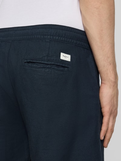 Mężczyzna nosi Relaxed Fit Chinoshorts aus Baumwoll-Leinen-Mix od Pepe Jeans, granatowy kolor, widoczna tylna kieszeń i label patch, tekstura bawełniano-lniana, ujęcie detailaufnahme tylnej części.
