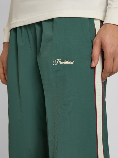 Männermodel trägt grüne Trackpants mit Label-Stitching Modell 'SLIPSTREAM' von PROHIBITED, seitlicher Streifen, Nahaufnahme Oberschenkel.