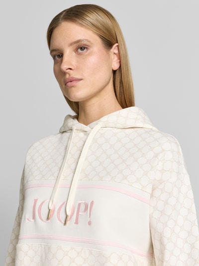 Kobiece model prezentuje Hoodie mit Label-Stitching Modell 'Tareli' od JOOP!, biały, wzór logo, bawełniany miks, krój relaxed fit, zbliżenie na górną część ciała.