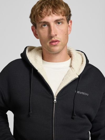 Männermodel trägt Regular Fit Sweatjacke aus Baumwoll-Mix mit Teddyfutter von REVIEW, Logo-Detail, Nahaufnahme Oberkörper.