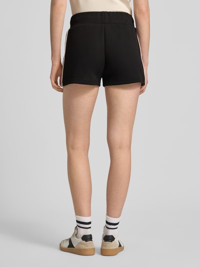 Vrouwenmodel draagt Shorts met koordsluiting en logo-print model 'BRITNEY' van Guess Activewear, katoenmix, loose fit, zwart, elastische tailleband, zijzakken, achteraanzicht volledig lichaam.