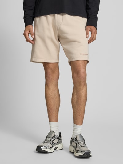 Männermodel trägt Regular Fit Shorts mit Logo-Stitching von Pegador aus Baumwoll-Mix in Beige mit elastischem Bund, Nahaufnahme Unterkörper.