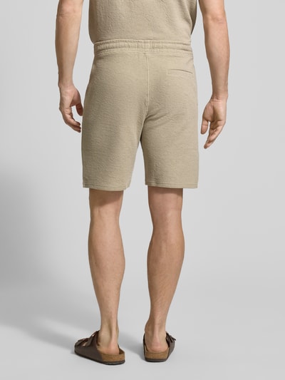 Männermodel trägt Sweatshorts mit elastischem Bund von MCNEAL in Beige mit Strukturmuster, Eingriff- und Gesäßtaschen, Ganzkörperansicht Rückansicht.