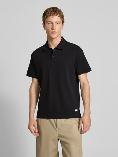 Männermodel trägt Regular Fit Poloshirt aus reiner Baumwolle von Tommy Jeans in Schwarz, unifarben, mit Logo, Ganzkörperansicht von vorne.
