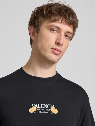 Männermodel trägt Relaxed Fit T-Shirt aus reiner Baumwolle Modell 'TASTY' von Only & Sons, schwarz, unifarben mit Schriftzug-Print, Nahaufnahme Oberkörper.