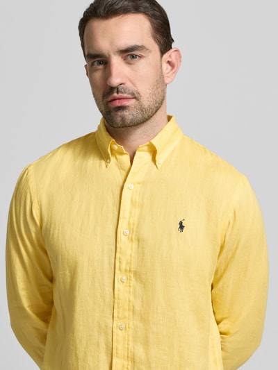 Mannenmodel draagt Regular Fit Freizeithemd aus reinem Leinen van Polo Ralph Lauren, geel, uni, flammégaren, logo detail, knoopsluiting, button-down kraag, lange mouw, pure linnen, close-up bovenlichaam vooraanzicht.