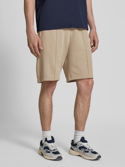 Männermodel trägt Bermudas mit elastischem Bund und Label-Stitching von CHAMPION, beigefarbener Baumwoll-Mix, Längsnähte, Regular Fit, Nahaufnahme Oberschenkel.