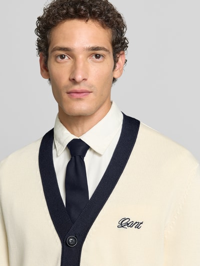 Männermodel trägt Regular Fit Strickjacke aus reiner Baumwolle von GANT in Creme mit dunkelblauen Details, Nahaufnahme Oberkörper.