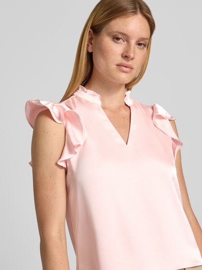 Frauenmodel trägt Blusentop aus Satin Modell 'Stella' von Neo Noir in zartem Rosa mit Rüschen, V-Ausschnitt und Stehkragen, Nahaufnahme Oberkörper. Material-Mix mit Stretch-Anteil, Regular Fit.